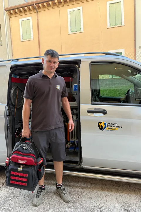 Il tecnico di Pronto Intervento Verona con la borsa degli attrezzi davanti al furgone attrezzato, con il logo sulla fiancata